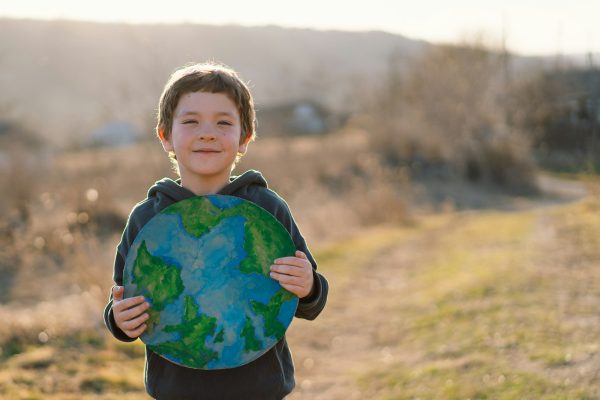 Little boy holding planet in hands against green spring background. Earth day